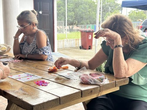 Dos mujeres adultas mayores se concentran en sus cartones de bingo sobre una mesa de madera durante el Bingotón Julio 2025.