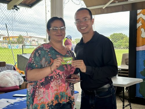 Ganadora con blusa colorida sostiene su tarjeta-premio junto al organizador durante el Bingotón Julio 2025