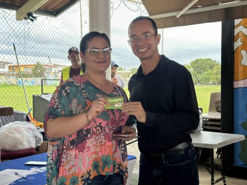 Ganadora con gafas y blusa estampada muestra su tarjeta-premio junto al organizador sonriendo en el Bingotón Julio 2025