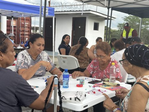 Cinco mujeres adultas juegan bingo y marcan fichas en una mesa blanca bajo carpas durante el Bingotón Julio 2025.