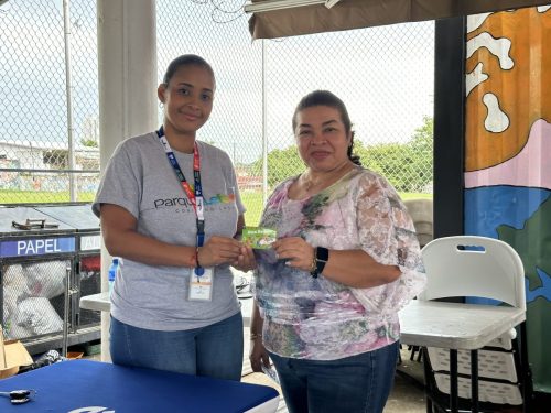 “Mujer del staff entrega una tarjeta-premio a la ganadora sonriente durante el Bingotón Julio 2025.”